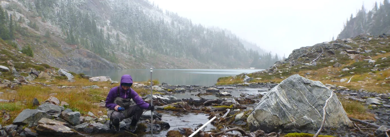 a student squats next to a mountain stream with electronic instruments