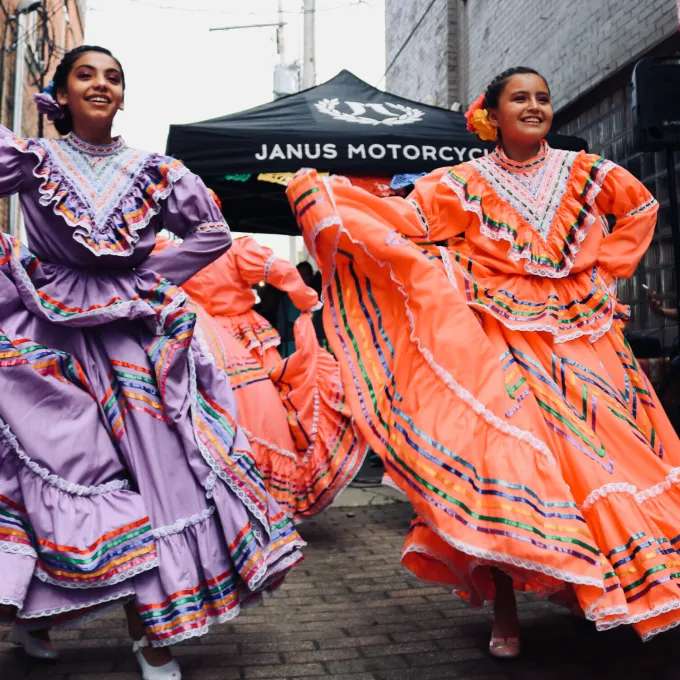 Two young Hispanic women dancing in traditional dresses. Photo by sydney Rae on Unsplash.